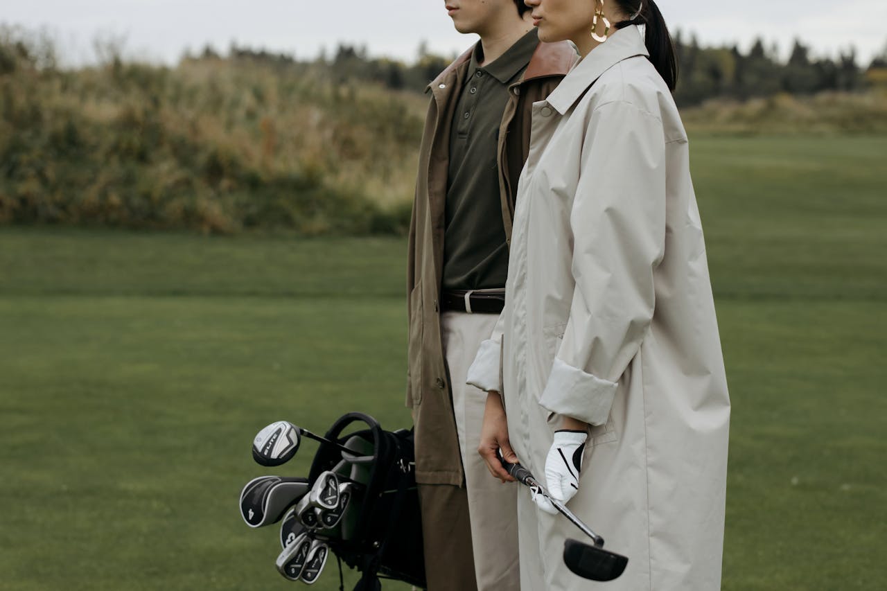 Elegant couple standing on a golf course with clubs, showcasing fashion and leisure lifestyle.